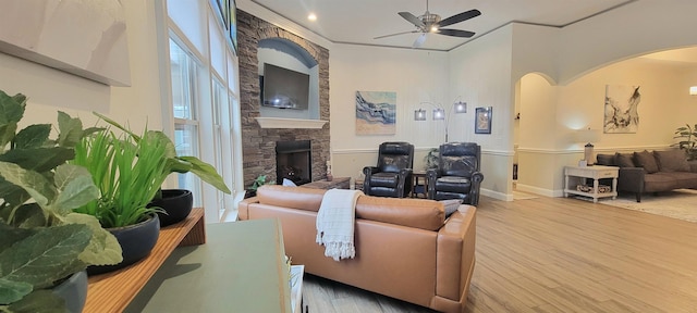 living room featuring ceiling fan, light hardwood / wood-style floors, a stone fireplace, and crown molding