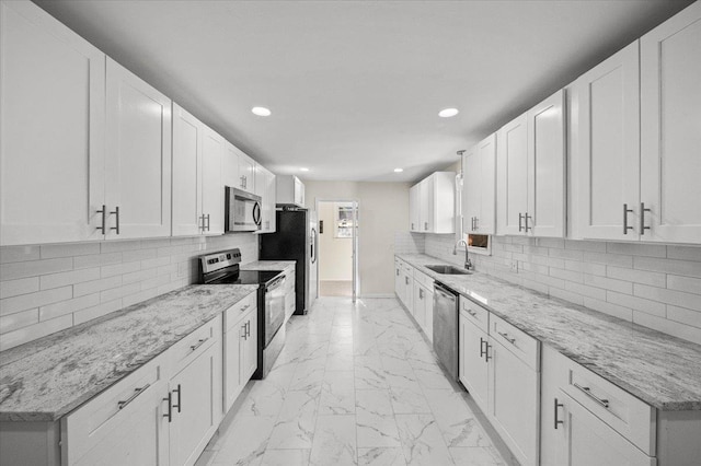 kitchen featuring light stone countertops, stainless steel appliances, white cabinetry, and sink