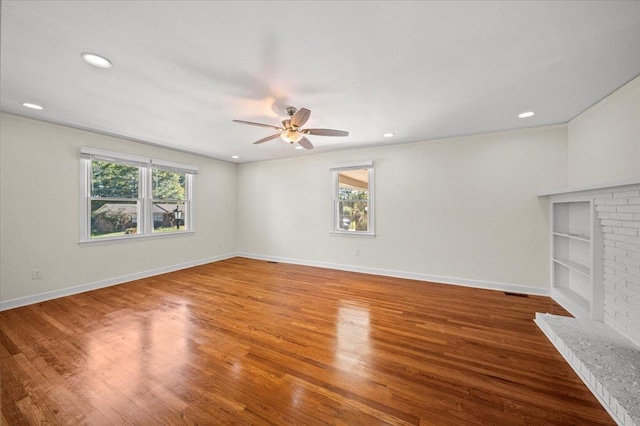 unfurnished living room featuring ceiling fan, hardwood / wood-style floors, a healthy amount of sunlight, and a brick fireplace