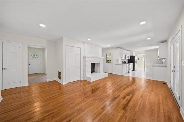 unfurnished living room with light hardwood / wood-style flooring, a brick fireplace, and sink