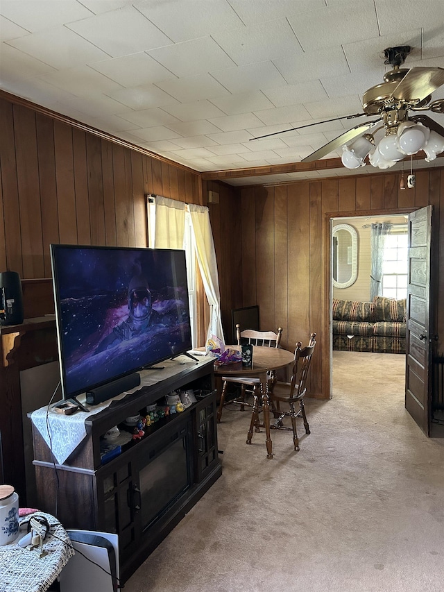 carpeted living room featuring ceiling fan and wooden walls