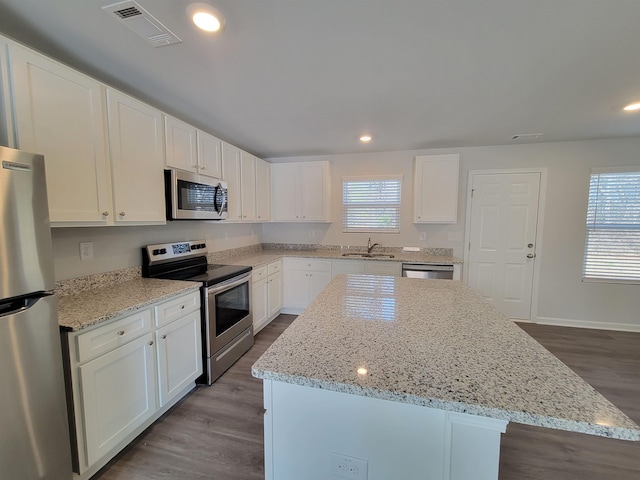 kitchen featuring light stone countertops, appliances with stainless steel finishes, sink, a center island, and white cabinetry