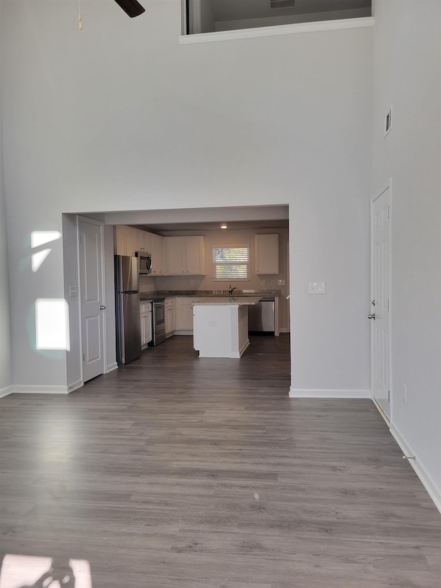 unfurnished living room with ceiling fan, light hardwood / wood-style floors, and a high ceiling