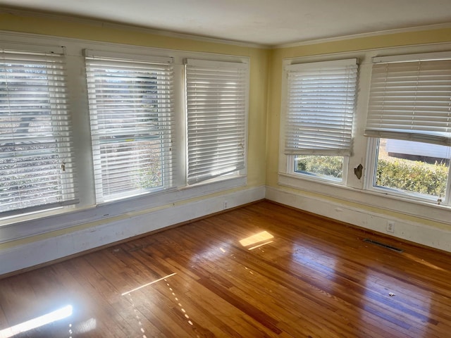 empty room featuring plenty of natural light, ornamental molding, and hardwood / wood-style flooring