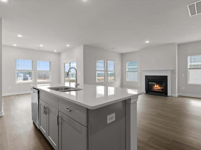 kitchen with sink, gray cabinets, light stone countertops, an island with sink, and stainless steel dishwasher