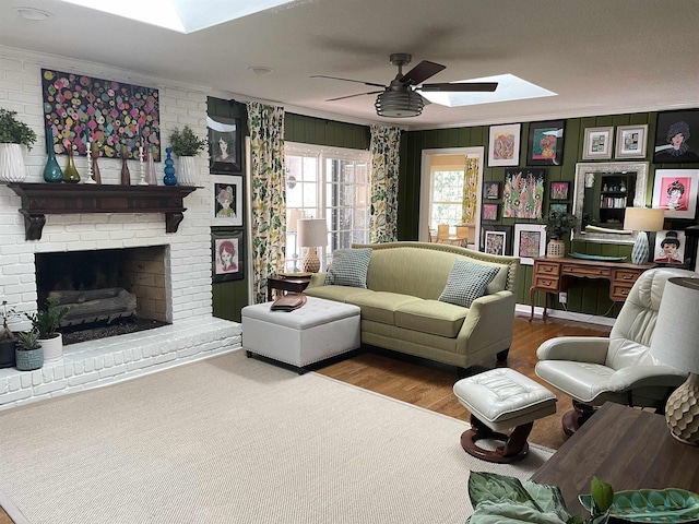 living room with a skylight, ceiling fan, a brick fireplace, hardwood / wood-style floors, and ornamental molding