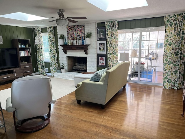 living room featuring ceiling fan, a skylight, wood-type flooring, and a brick fireplace