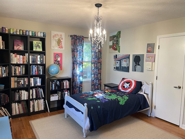 bedroom with wood-type flooring, a textured ceiling, and an inviting chandelier