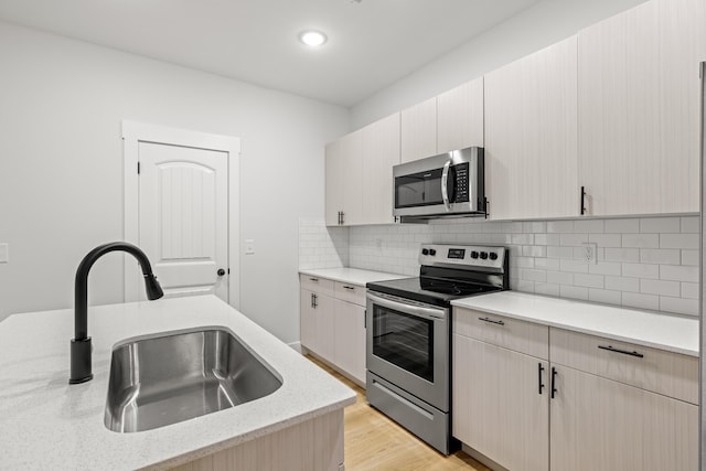 kitchen featuring sink, decorative backsplash, light stone countertops, light hardwood / wood-style floors, and stainless steel appliances