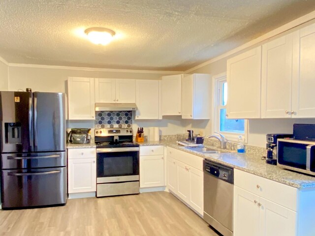 kitchen with appliances with stainless steel finishes, light wood-type flooring, ornamental molding, sink, and white cabinetry