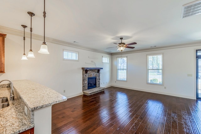 unfurnished living room featuring a stone fireplace, ceiling fan, sink, and ornamental molding