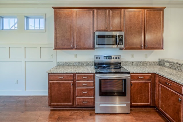 kitchen with light stone countertops, appliances with stainless steel finishes, dark hardwood / wood-style flooring, and ornamental molding