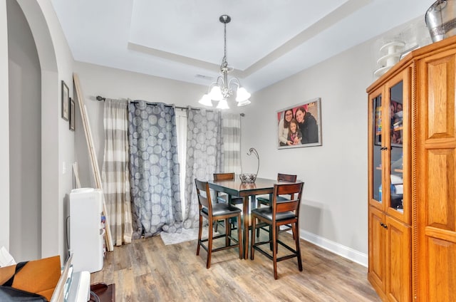 dining space featuring a raised ceiling, a chandelier, and light hardwood / wood-style floors