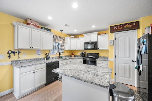 kitchen featuring pendant lighting, black appliances, white cabinets, sink, and light stone counters