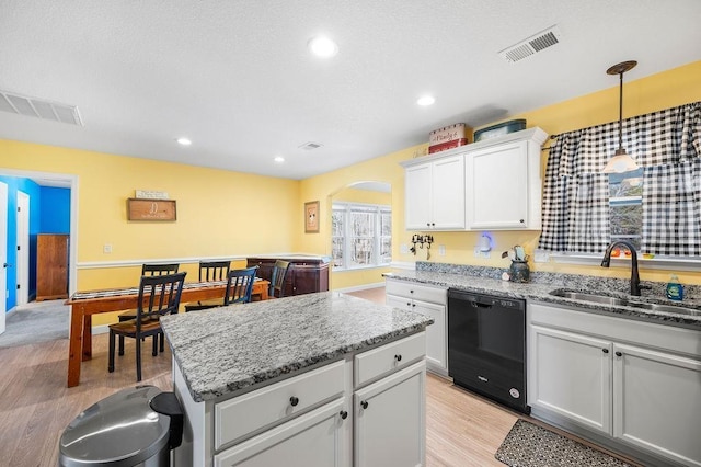 kitchen with white cabinets, sink, hanging light fixtures, light wood-type flooring, and black dishwasher