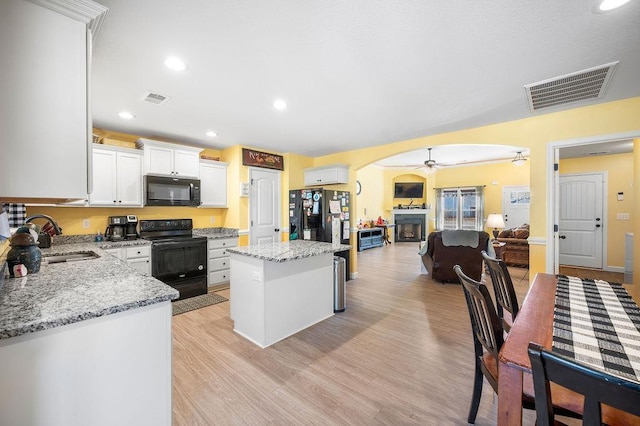 kitchen featuring light stone counters, sink, black appliances, white cabinets, and a center island