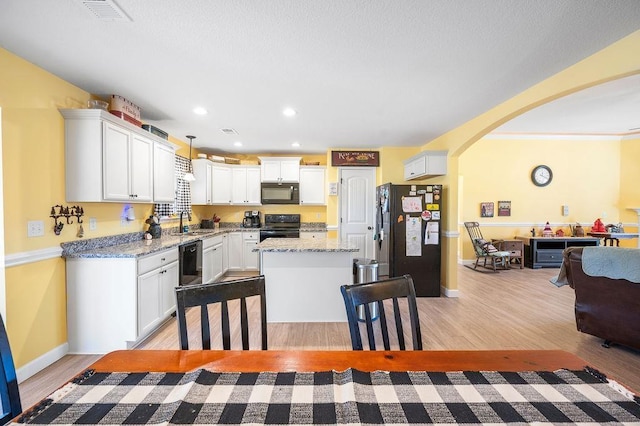 kitchen with light stone countertops, sink, black appliances, a kitchen island, and hanging light fixtures