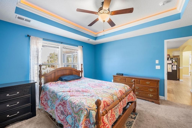 carpeted bedroom with a tray ceiling, ceiling fan, and crown molding