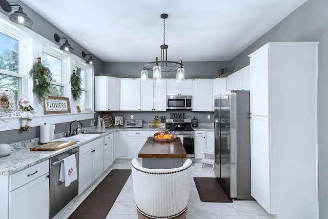 kitchen with a center island, sink, stainless steel appliances, pendant lighting, and white cabinets