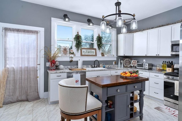 kitchen with sink, hanging light fixtures, wooden counters, white cabinets, and appliances with stainless steel finishes