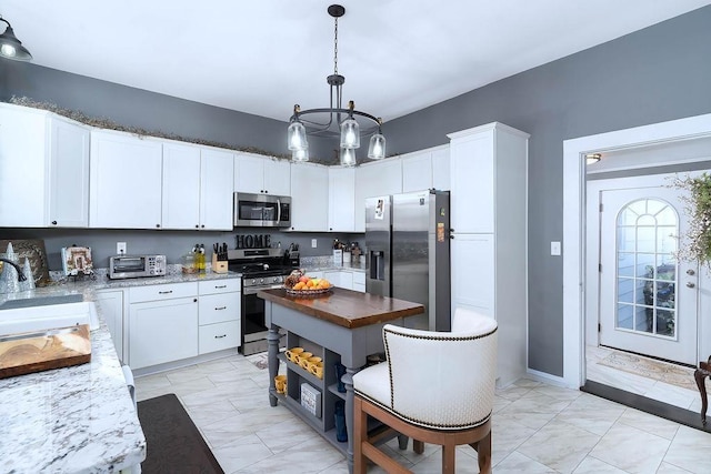 kitchen featuring appliances with stainless steel finishes, white cabinetry, hanging light fixtures, and dark stone counters