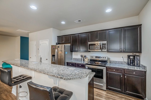 kitchen with a breakfast bar, dark brown cabinets, stainless steel appliances, and a kitchen island with sink