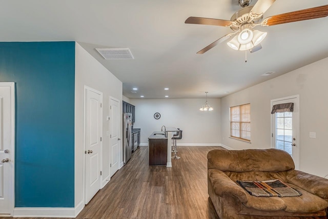 living room with ceiling fan with notable chandelier, sink, and dark wood-type flooring