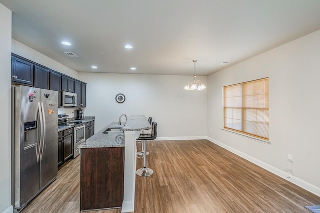 kitchen with light stone countertops, hardwood / wood-style floors, a chandelier, decorative light fixtures, and appliances with stainless steel finishes