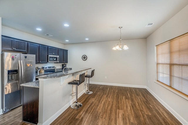 kitchen with a kitchen bar, appliances with stainless steel finishes, light stone countertops, a chandelier, and hanging light fixtures