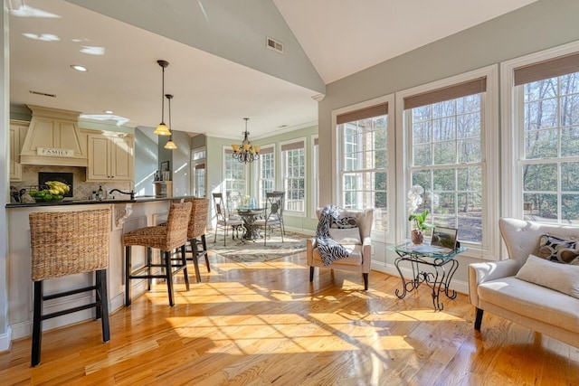 kitchen with backsplash, an inviting chandelier, cream cabinetry, decorative light fixtures, and a breakfast bar area