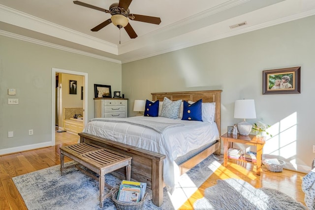 bedroom with a raised ceiling, crown molding, ceiling fan, connected bathroom, and light hardwood / wood-style floors