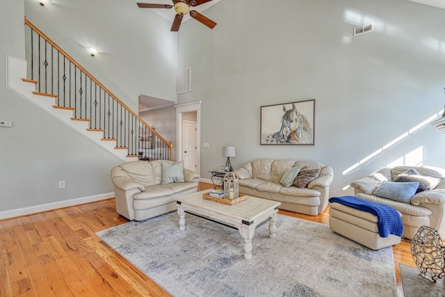 living room featuring ceiling fan, a towering ceiling, and light wood-type flooring