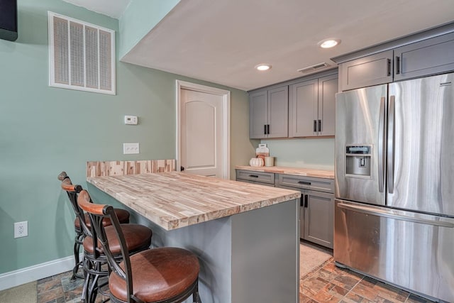 kitchen featuring wooden counters, stainless steel refrigerator with ice dispenser, a breakfast bar, a center island, and gray cabinets