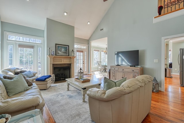 living room with french doors, light hardwood / wood-style flooring, high vaulted ceiling, and a healthy amount of sunlight