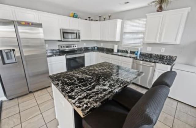 kitchen featuring white cabinets, sink, dark stone countertops, light tile patterned floors, and appliances with stainless steel finishes