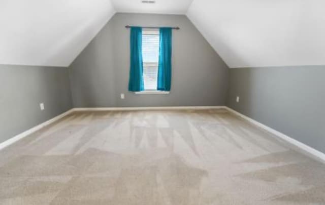 bonus room with light colored carpet and vaulted ceiling