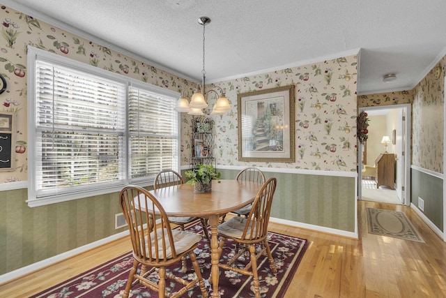 dining area with a textured ceiling, light hardwood / wood-style floors, crown molding, and a chandelier