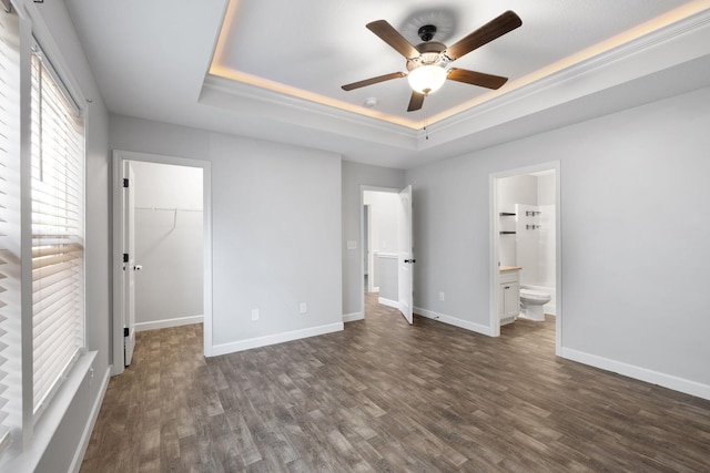 unfurnished bedroom featuring a walk in closet, ensuite bath, a raised ceiling, ceiling fan, and a closet