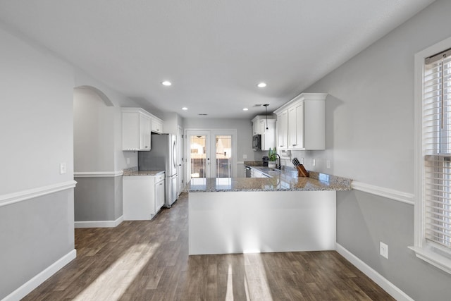 kitchen with stainless steel refrigerator, kitchen peninsula, plenty of natural light, and white cabinets