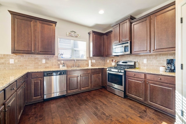 kitchen with backsplash, sink, dark hardwood / wood-style floors, light stone counters, and stainless steel appliances