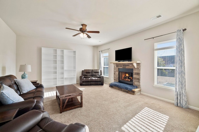 living room featuring carpet flooring, a stone fireplace, plenty of natural light, and ceiling fan