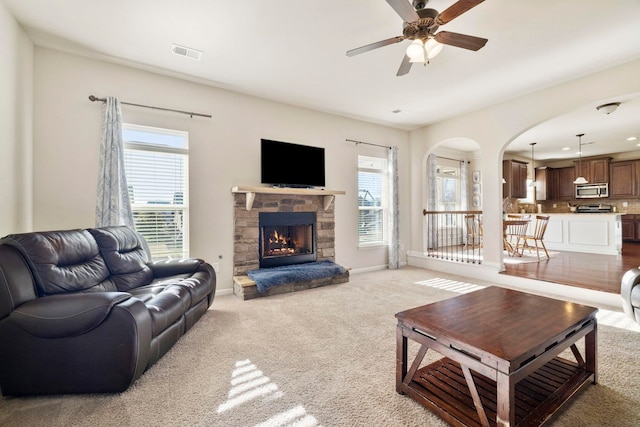 carpeted living room featuring a stone fireplace, a wealth of natural light, and ceiling fan