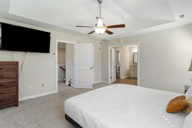 bedroom featuring a tray ceiling, light colored carpet, ceiling fan, and ensuite bath