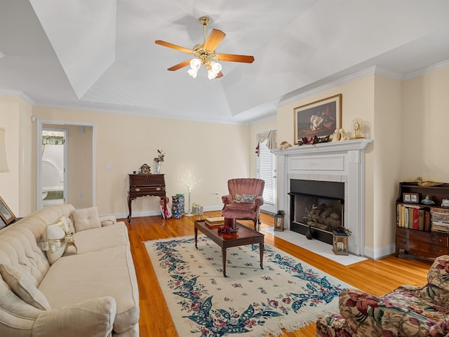 living room featuring a raised ceiling, a tiled fireplace, ornamental molding, and light wood-type flooring