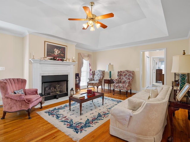 living room featuring ornamental molding, a tray ceiling, ceiling fan, light hardwood / wood-style flooring, and a tiled fireplace