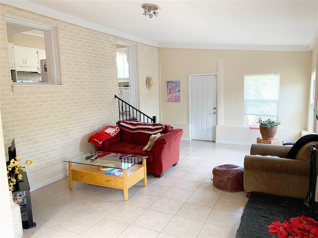 tiled living room featuring plenty of natural light, ornamental molding, and brick wall