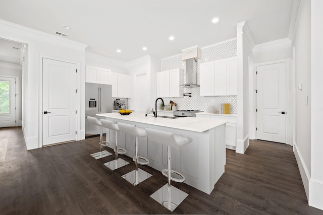 kitchen featuring sink, wall chimney range hood, high end refrigerator, a kitchen bar, and a center island with sink