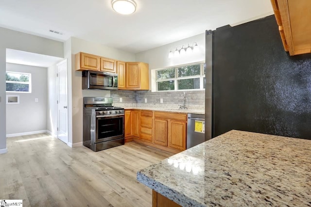 kitchen featuring light wood-type flooring, tasteful backsplash, light stone counters, stainless steel appliances, and sink