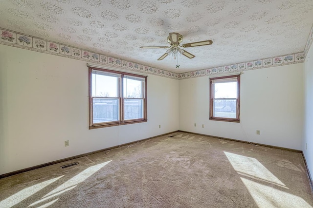 empty room with light carpet, plenty of natural light, ceiling fan, and a textured ceiling