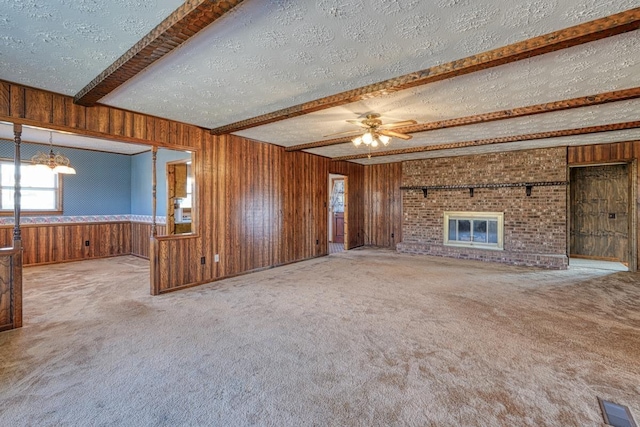 unfurnished living room featuring a brick fireplace, ceiling fan with notable chandelier, a textured ceiling, light colored carpet, and beamed ceiling